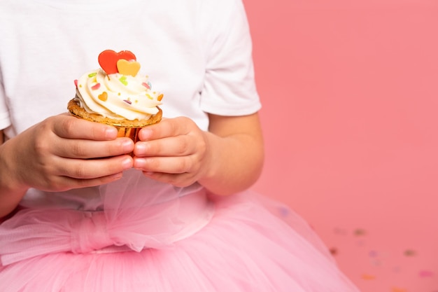 Une fille en tutu rose tient un petit gâteau avec un cœur dessus.