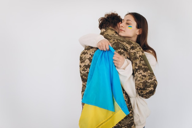 Une fille ukrainienne embrasse et tient un drapeau jaune et bleu d'un militaire en uniforme et lui dit au revoir