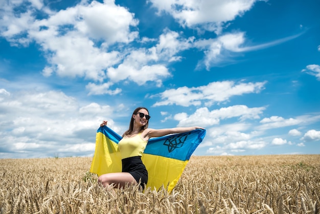 Fille ukrainienne de mode avec le drapeau national sur le champ de blé en été