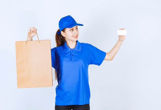 Fille en uniforme bleu tenant un sac à provisions en carton et présentant sa carte de visite.