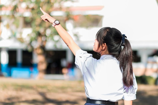 Une fille en uniforme d'école thaïlandaise est debout, le dos et l'index pointé vers le ciel.