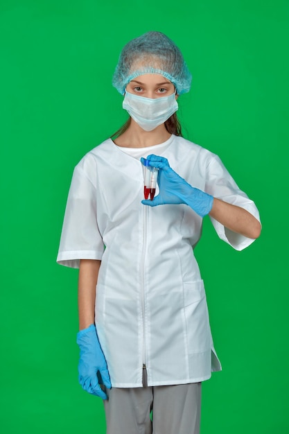 Une fille en uniforme médical sur fond vert avec des tubes à essai avec du sang