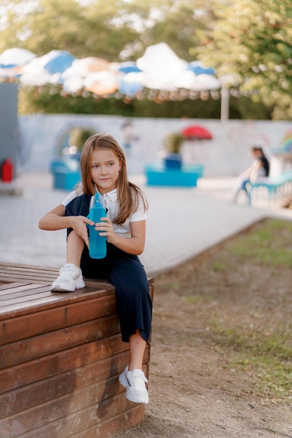 une fille en uniforme scolaire avec une bouteille d'eau est assise dans le parc