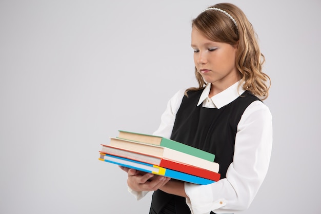 Une fille en uniforme scolaire regarde tristement une pile de manuels qu'elle tient dans ses mains