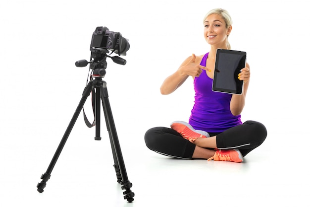 Fille en uniforme de sport est assis devant la caméra avec tablette sur fond blanc