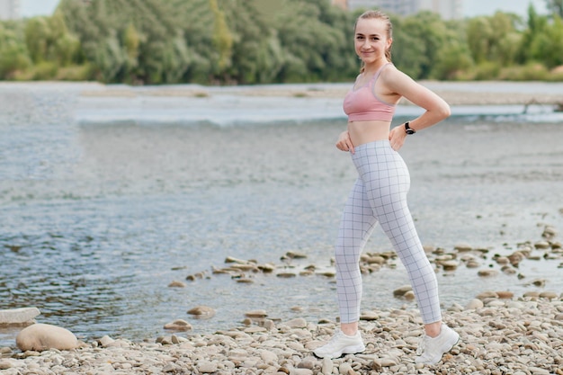 Fille en uniforme de sport fait un étirement sur la rive du fleuve