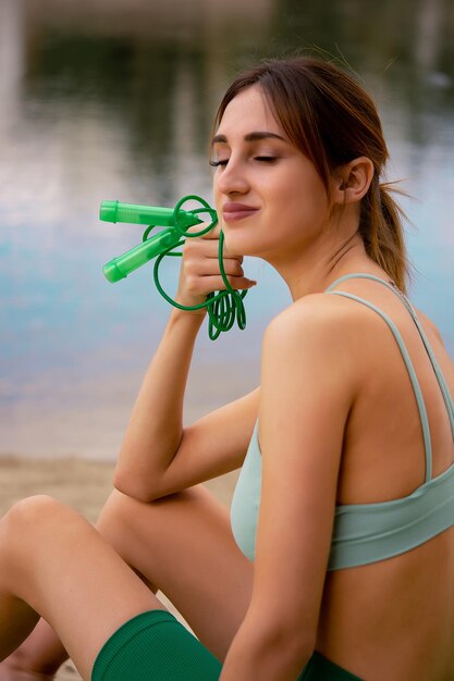 une fille en uniforme de sport tient une corde à sauter dans ses mains, vêtue d'un haut de survêtement vert