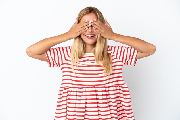 Fille uruguayenne blonde isolée sur fond blanc couvrant les yeux par les mains et souriant