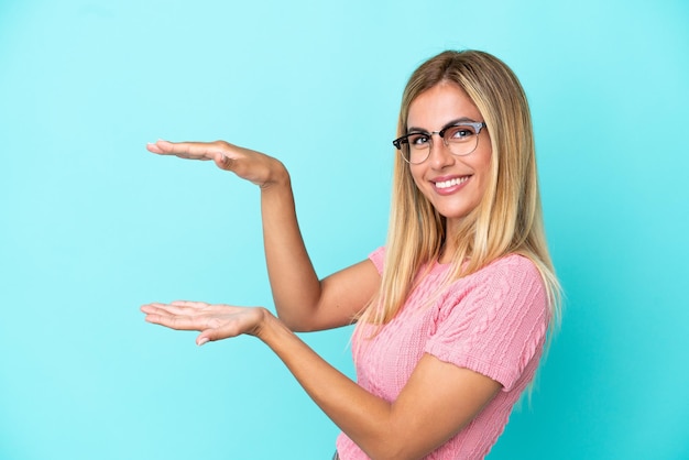 Fille uruguayenne blonde isolée sur fond bleu tenant un espace pour insérer une annonce