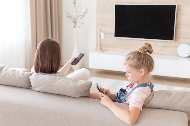 Fille utilisant un téléphone intelligent assise à côté de sa mère sur le canapé à la maison