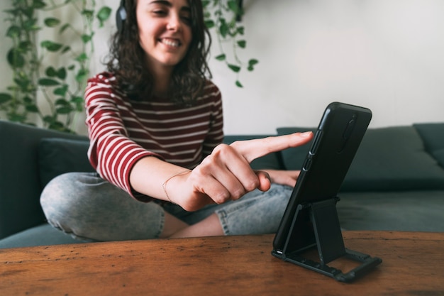 Fille utilisant un téléphone intelligent avec un casque assis sur un canapé à la maison. Concept de séjour à la maison