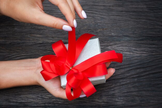 Photo la fille va dénouer le nœud rouge de la boîte cadeau à la main.