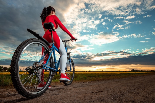 Fille sur un vélo sur le fond du coucher du soleil