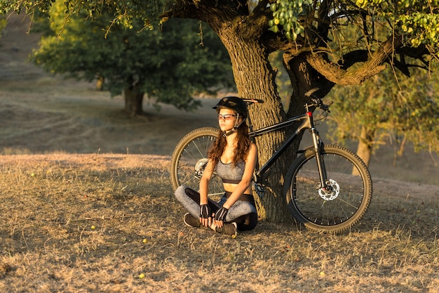 Fille sur un vélo de montagne sur tout-terrain beau portrait d'un cycliste au coucher du soleil