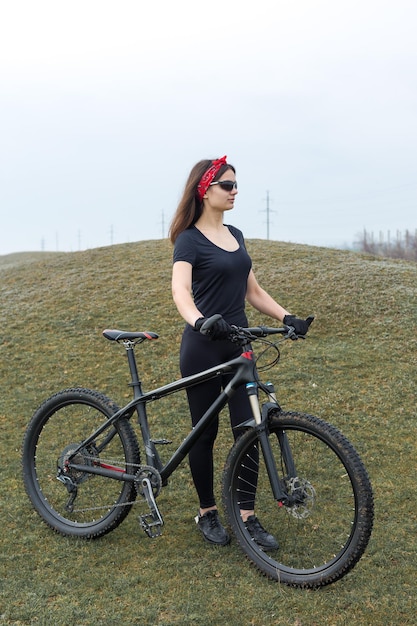 Fille sur un vélo de montagne sur tout-terrain beau portrait d'un cycliste par temps de pluie Fille de remise en forme monte un vélo de montagne moderne en fibre de carbone en vêtements de sport Portrait en gros plan d'une fille en bandana rouge