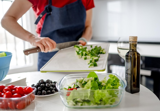 Photo une fille verse des concombres hachés dans un bol pour une salade grecque à la maison dans une cuisine lumineuse