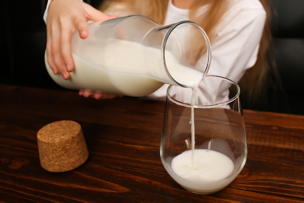 Une fille verse du lait d'une bouteille dans un verre, une source de calcium.