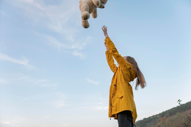 Fille en veste jaune avec ours en peluche sur fond de ciel