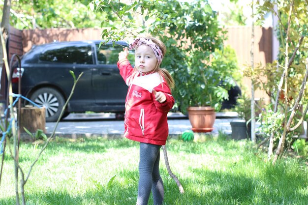 Une fille en veste rouge joue dans l'herbe.