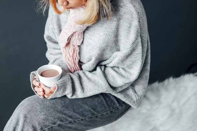 Une fille avec des vêtements d'hiver dégustant une tasse de chocolat chaud en hiver à la maison