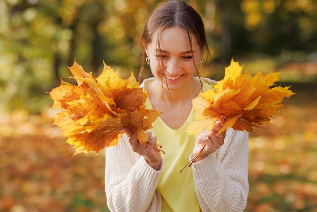 Fille en vêtements jaunes dans le parc d'automne se réjouit en automne tenant des feuilles jaunes dans ses mains au chaud