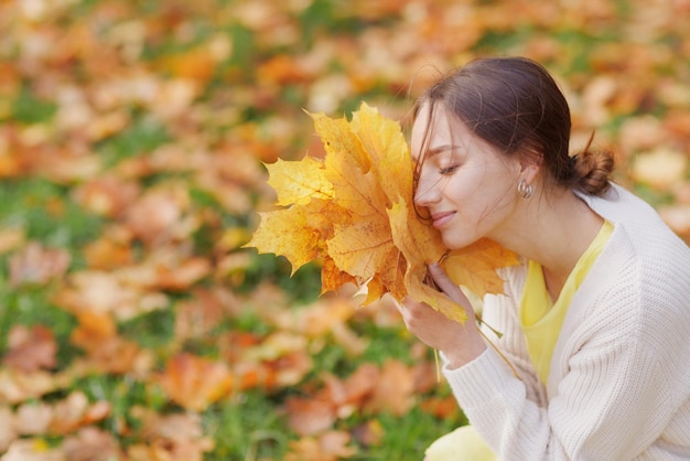 une fille en vêtements jaunes dans un parc d'automne se réjouit en automne tenant des feuilles jaunes dans ses mains
