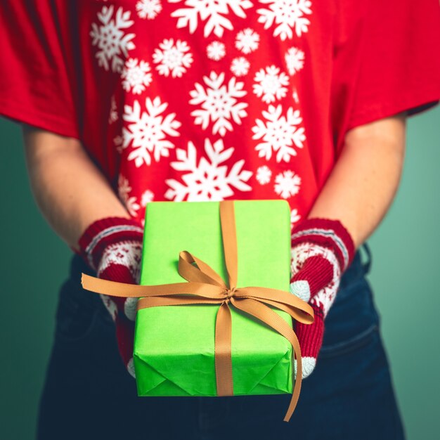 Fille en vêtements avec un ornement de Noël tient une boîte-cadeau