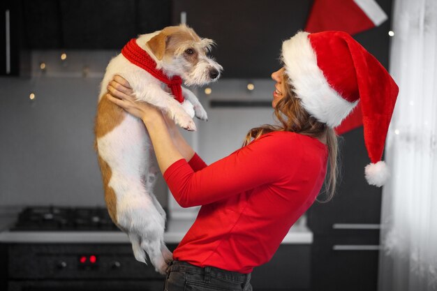 Fille en vêtements rouges et jack russell terrier jouent dans la cuisine le soir de noël