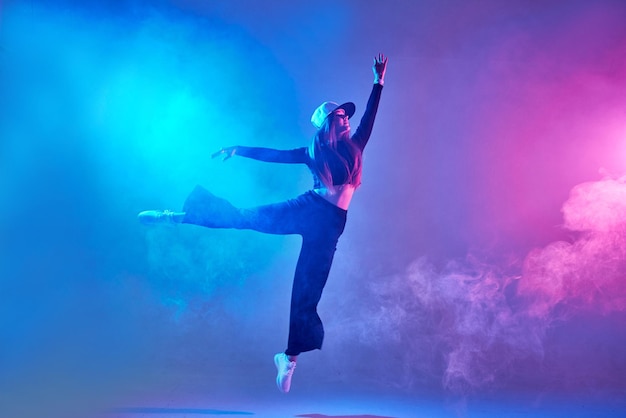 Une fille en vêtements sombres danse sur un fond de néon dans la danse moderne de fumée