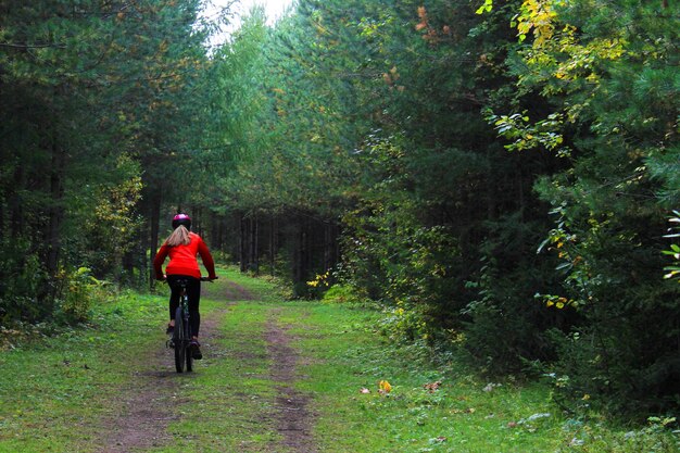 Une fille en vêtements de sport et un casque fait du vélo à travers la forêt Vue arrière