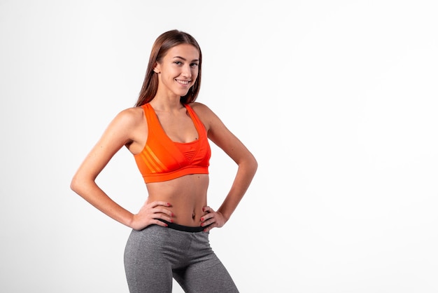 Une fille en vêtements de sport se tient sur le côté sur un fond blanc et sourit au concept de mode de vie sain de l'appareil photo