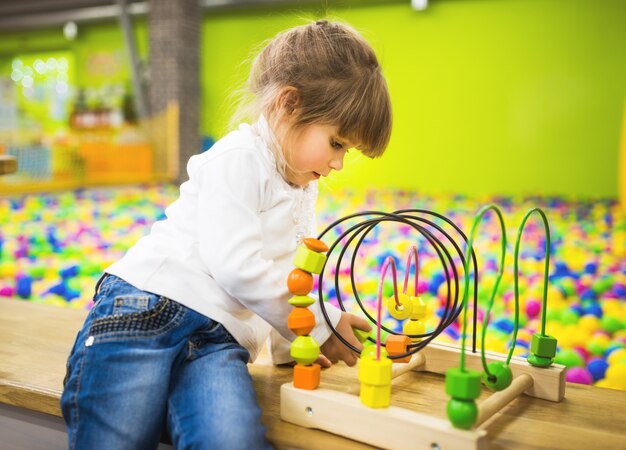 Une fille vêtue d'un jean et d'un pull blanc joue avec un jouet en bois en développement dans la salle de jeux.