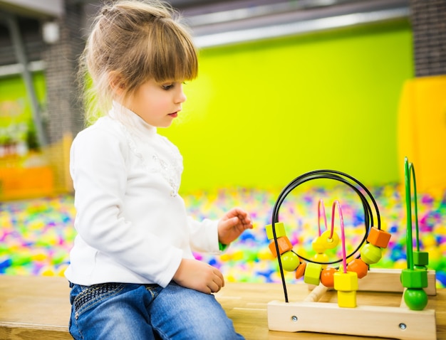 Une fille vêtue d'un jean et d'un pull blanc joue avec un jouet en bois en développement dans la salle de jeux