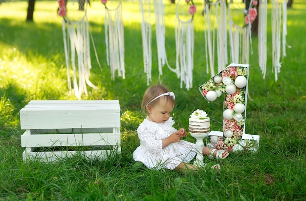 Une fille vêtue d'une robe blanche élégante est assise sur l'herbe et regarde ses mains souillées de crème