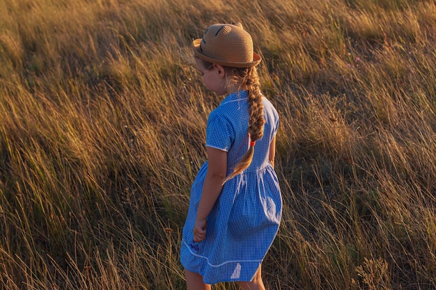 Une fille vêtue d'une robe bleue se promène dans un champ d'herbes hautes.