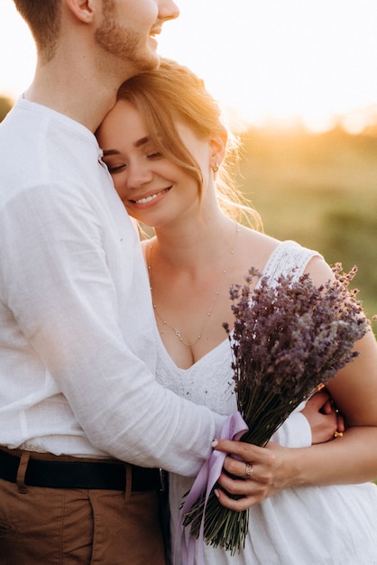 Fille vêtue d'une robe d'été blanche et un gars vêtu d'une chemise blanche lors d'une promenade au coucher du soleil avec un bouquet dans un village en dehors de la ville