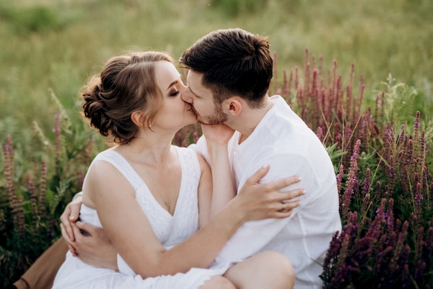 Fille vêtue d'une robe d'été blanche et un gars vêtu d'une chemise blanche lors d'une promenade au coucher du soleil avec un bouquet dans un village en dehors de la ville