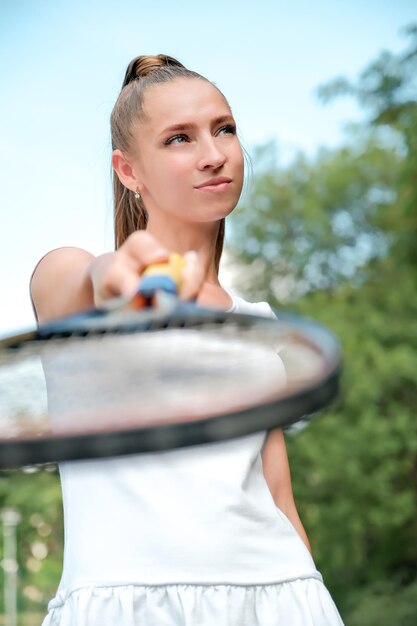 Une fille vêtue d'une robe de sport blanche se tient sur un court de tennis et tient un portrait de raquette d'une fille sur le court de tennis