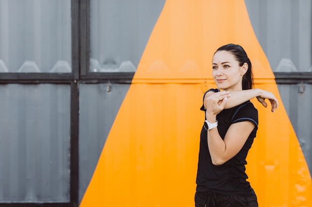 Fille vêtue d'un T-shirt noir et d'un short, s'échauffant avant de courir sur un mur gris jaune