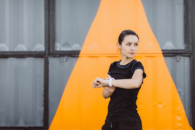 Fille vêtue d'un T-shirt noir et d'un short, s'échauffant avant de courir sur un mur gris jaune