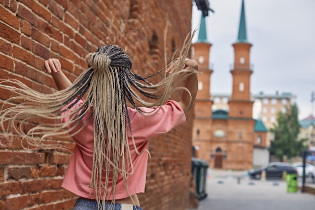 Une fille vêtue d'un t-shirt rose avec de longues dreadlocks qui volent dans différentes directions se tient debout avec le dos...