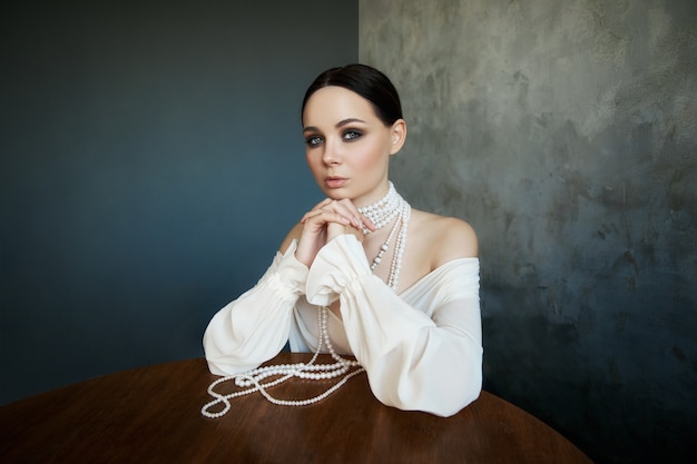 Fille vêtue de vêtements boho blancs avec des perles de perles blanches autour du cou est assise à une table