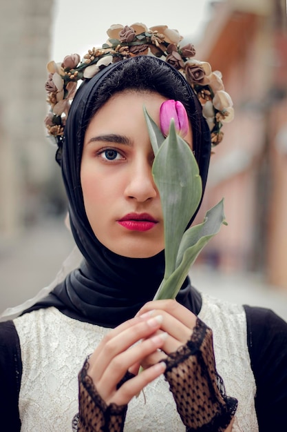 Une fille voilée met une couronne de roses sur sa tête et tient une fleur couvrant la moitié de son visage