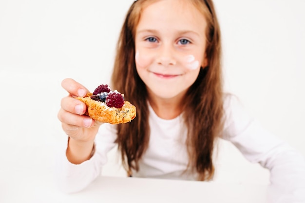 Fille vous traitant avec un espace libre de gâteau aux baies Petite lassie souriante propose un biscuit sucré à la caméra Boulangerie maison concept de pâtisserie culinaire pour enfants