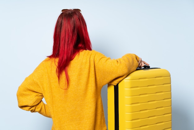 Fille de voyageur tenant une valise sur le mur bleu en position arrière