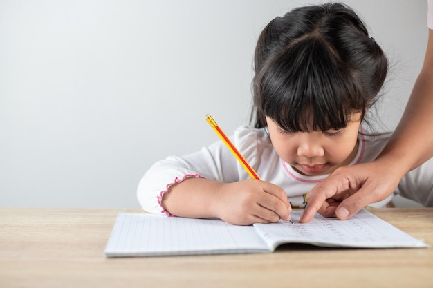 Les filles asiatiques âgées de 45 ans ont de l'aide de maman pour les devoirs des enfants tenant des crayons et écrivant des devoirs