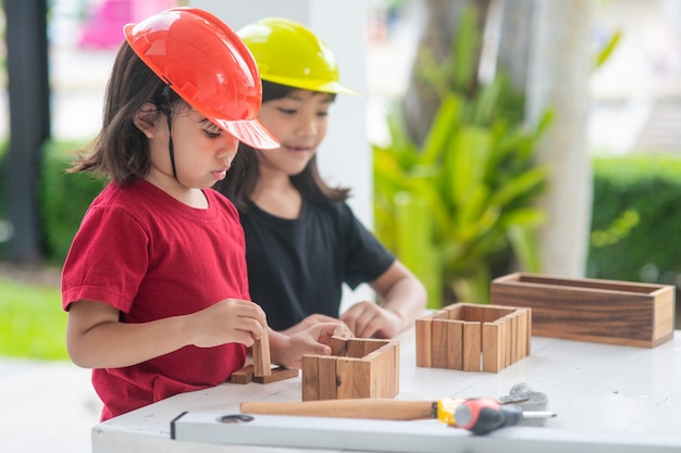 Filles asiatiques de la fratrie portant des chapeaux d'ingénierie construisant une maison à partir du jouet en bois.