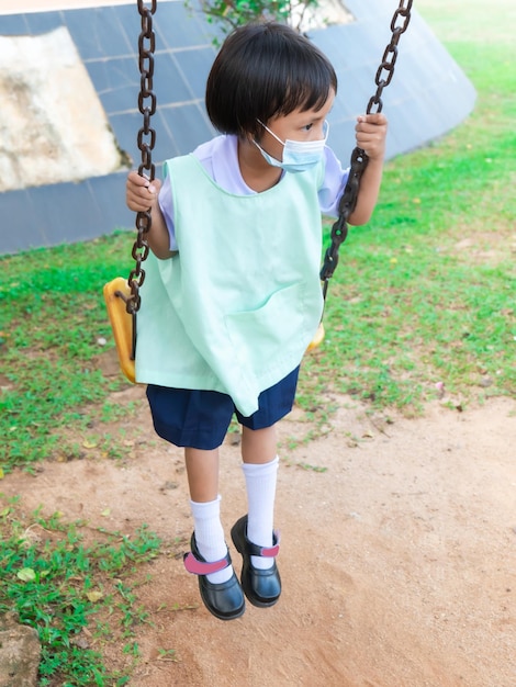 Des filles asiatiques portant des masques en uniforme scolaire sortent pour faire des activités Amusez-vous à jouer sur les balançoires