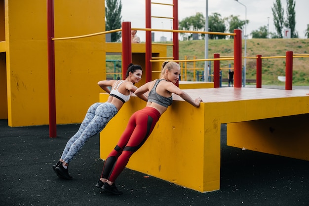 Les filles athlétiques et sexy font des push-UPS à l'extérieur de manière synchrone. Fitness, mode de vie sain