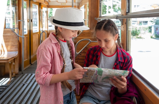 Des filles brunes de plusieurs années et des voyageurs de plusieurs années marchant dans un vieux tramway regardant une carte et des sites touristiques